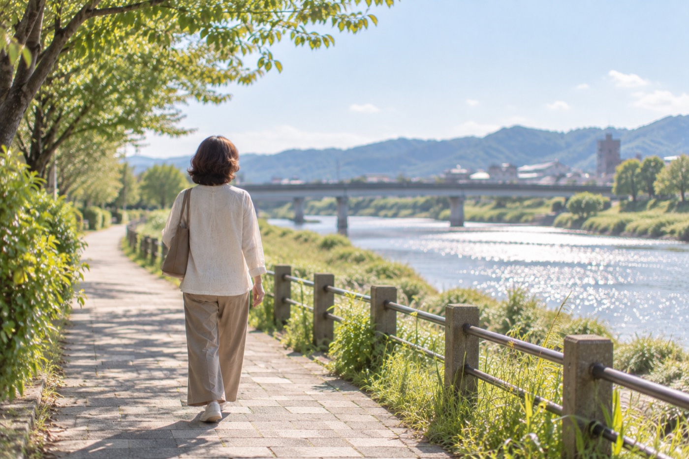 川沿いの道を一人で歩く女性の後ろ姿